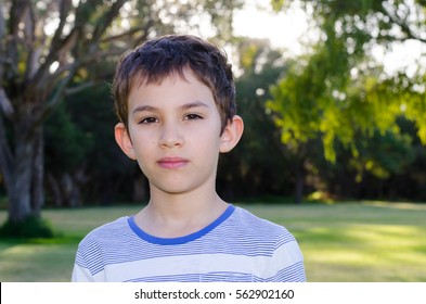 Portrait Young Hispanic Or Latino Boy Outdoor In Park, With Sad Serious Thoughtful Facial Expression, Copy Space, Blurred Background.