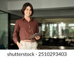 Portrait of young Hispanic professional business woman standing in office. Happy female company executive, smiling businesswoman entrepreneur corporate leader manager looking at camera using tablet.