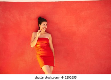 Portrait Of Young Hispanic Woman Smoking E-cig Leaning On Red Wall With Copy Space.