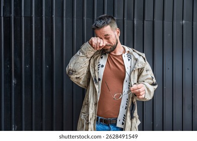 Portrait of young homeless man standing against black wall in the alley. Homelessness and abandoned social issue concept.