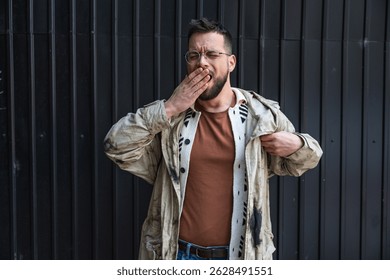 Portrait of young homeless man standing against black wall in the alley. Homelessness and abandoned social issue concept.