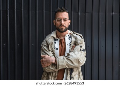 Portrait of young homeless man standing against black wall in the alley. Homelessness and abandoned social issue concept.