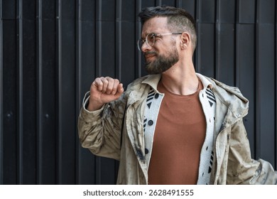 Portrait of young homeless man standing against black wall in the alley. Homelessness and abandoned social issue concept.