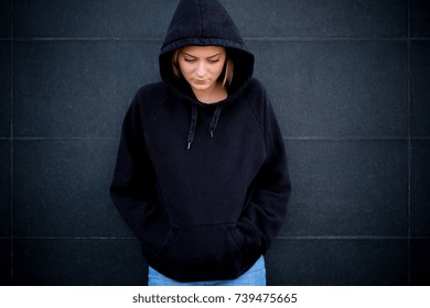Portrait of young hooded girl on black background wall