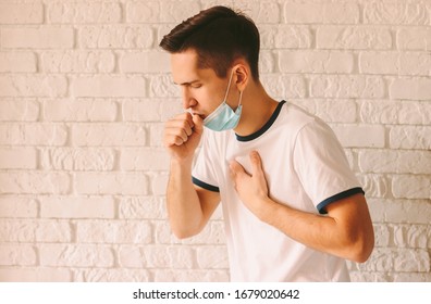 Portrait young ill man in medical protective face mask coughing or sneezing a lot and feeling bad. Sick man patient with chest pain. Symptoms of pandemic coronavirus COVID-19, flu, cold or pneumonia