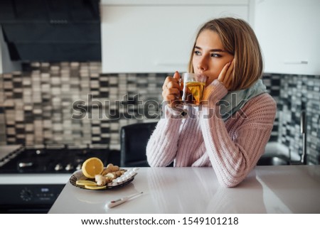Portrait of young ill woman drinking cup of hot tea at home kitchen.