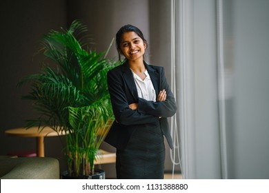 Portrait Of A Young Indian Asian Business Woman Standing By The Window In A Meeting Room, Smiling With Her Arms Crossed. She Looks Confident, Happy And Optimistic. 