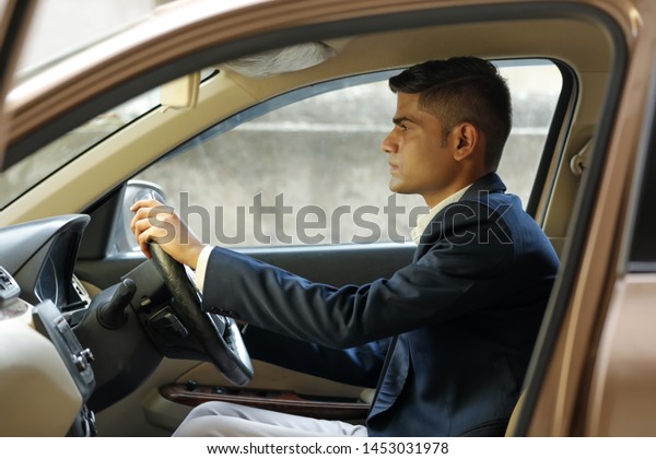 Portrait of\
young Indian business man, driving a\
car