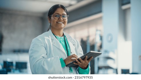 Portrait of Young Indian Female Specialist in a Lab Coat Smiling and Using Laptop Computer. Professional and Successful Woman Working as an Engineer, Thinking and Developing High Tech Projects
