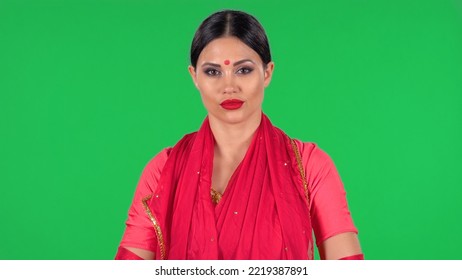 Portrait Of A Young Indian Girl With Red Bindi Dot In National Classic Red Sari Looking Straight. A Brunette With Long Hair And Red Lips On Green Screen At Studio.