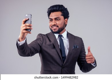 Portrait Of Young Indian Man In A Stylish Classic Suit Making Video Call From The Phone On White Background In Studio.