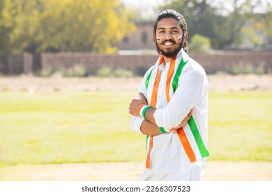 Portrait of young indian man wearing traditional white kurta and tricolor duppata standing cross arms at park. Election and politics, celebrating Independence day or Republic day. - Powered by Shutterstock