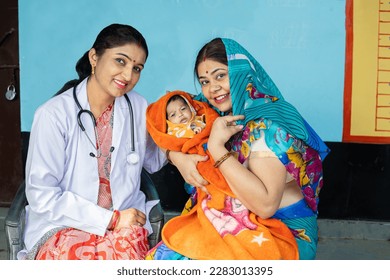 Portrait of Young indian pediatrician doctor sitting with Mother and her new born baby looking at camera, Rural healthcare camp concept. - Shutterstock ID 2283013395