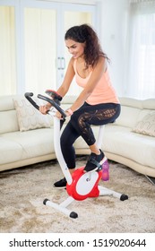 Portrait Of Young Indian Woman Doing A Workout With An Exercise Bike In The Living Room. Shot At Home