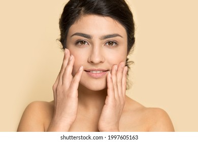 Portrait Of Young Indian Woman Isolated On Yellow Studio Background Touch Healthy Face Skin After Beauty Salon Procedures. Smiling Mixed Race Female Satisfied With Facial Treatment. Skincare Concept.