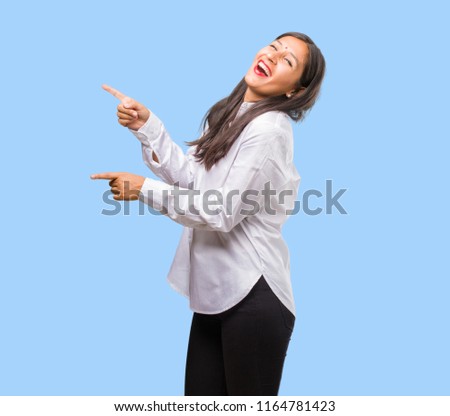 Portrait of a young indian woman pointing to the side, smiling surprised presenting something, natural and casual