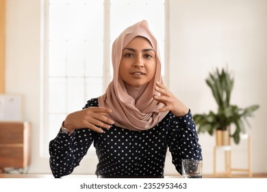 Portrait of young indian woman wearing hijab sit at desk talk on video call have interview conversation online, millennial Arabic ethnic female engaged in webcam virtual conference in office - Powered by Shutterstock