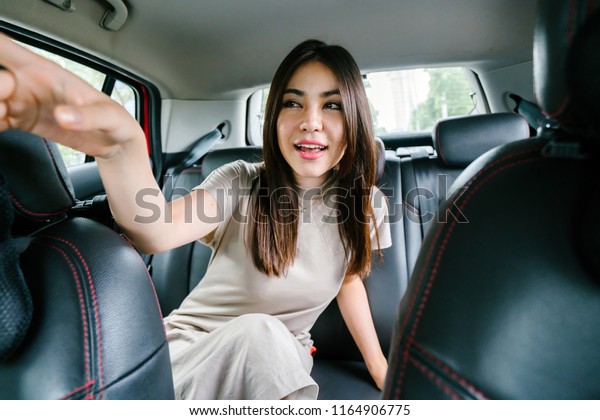 Portrait of a young Japanese Asian woman sitting in the\
back seat of a car vehicle and leaning forwards to point at the\
street. She is giving directions to the driver as she reaches her\
destination. 