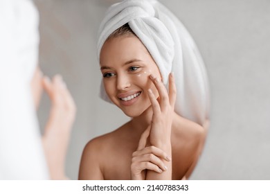 Portrait of young lady applying nourishing eye cream after shower, looking at mirror and smiling in bathroom interior. Anti-aging cosmetics, tools against lines, wrinkles eye care concept - Powered by Shutterstock