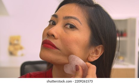 PORTRAIT: Young Lady Massaging Her Face With Gua Sha Scraper For Facial Lifting. Beautiful Asian Woman Using Gua Sha Scraper For Rejuvenating Anti-aging Massage And Facial Muscles Relief Treatment.