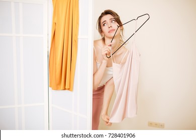 Portrait Of Young Lady Standing With T-shirt On Hanger In Hand And Tiredly Looking Aside Out Of Fitting Room While Waiting Clothes Assistant In Fashion Store 