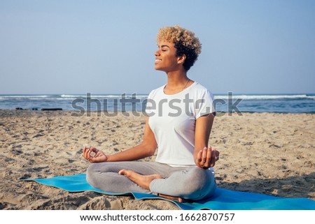 Portrait of a young latin african woman sitting in yoga pose at the beach lifestyle