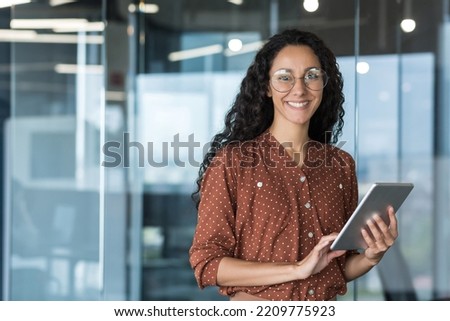 Portrait of a young Latin American woman journalist. He is standing in the office, holding a tablet