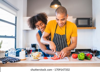 Portrait of young latin couple cooking together in the kitchen at home. Relationship, cook and lifestyle concept. - Powered by Shutterstock