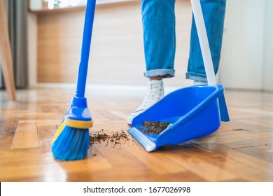 Portrait of young latin man sweeping wooden floor with broom at home. Cleaning, housework and housekeeping concept.