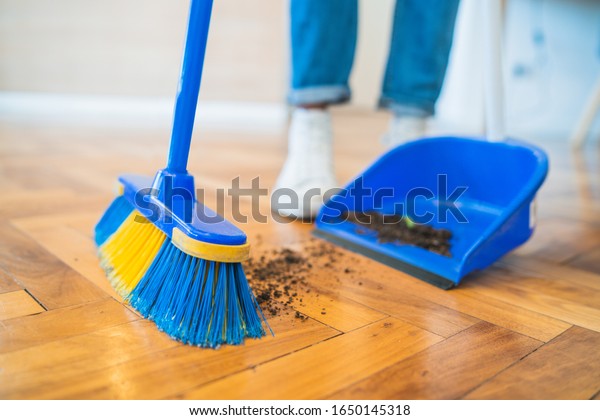 Portrait of\
young latin man sweeping wooden floor with broom at home. Cleaning,\
housework and housekeeping\
concept.