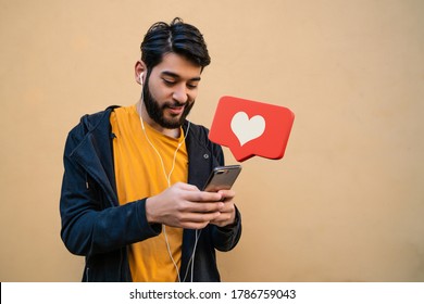 Portrait Of Young Latin Man Using His Mobile Phone. Red Heart Like Notification. Social Media And Communication Concept.