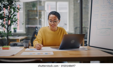 Portrait of Young Latin Marketing Specialist in Glasses Working on Laptop Computer in Busy Creative Office Environment. Beautiful Diverse Multiethnic Female Project Manager is Browsing Internet.