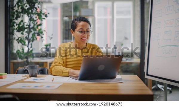 Portrait of Young Latin Marketing Specialist in\
Glasses Working on Laptop Computer in Busy Creative Office\
Environment. Beautiful Diverse Multiethnic Female Project Manager\
is Browsing Internet.
