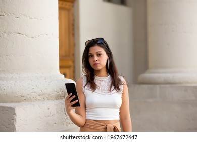 A portrait of young latin receiving a message on her smartphone in the street