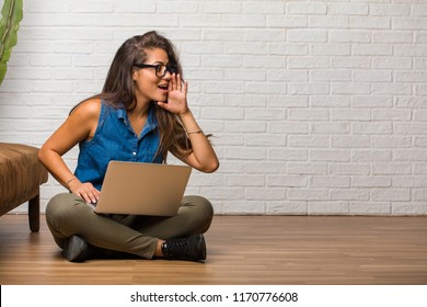 Portrait of young latin woman sitting on the floor whispering gossip undertone, trying not to be heard, is warning of a possible weakness or an opportunity. Holding a laptop. - Shutterstock ID 1170776608
