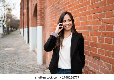 Portrait of young latin woman talking on the phone outdoors in the street. Urban concept. - Shutterstock ID 1748256779