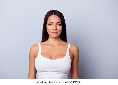 Portrait of a young latino american woman. She is in a casual white singlet standing on the pure light blue background