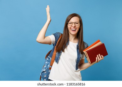 Portrait of young laughing cute woman student in glasses with backpack spreading raising hand up holding school books isolated on blue background. Education in high school university college concept - Shutterstock ID 1183165816