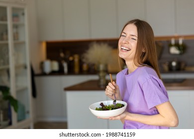 Portrait Of Young Laughing Woman With Plate Of Fresh Salad Standing At Home Kitchen, Happy Smiling Beautiful Girl Eating Healthy Green Salad Indoors, Healthy Lifestyle