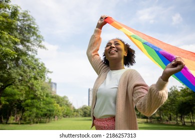 Portrait of young lesbian woman waving pride rainbow flag in their backs supporting LGBTQ pride in the park. Independence and gender diversity. Supporters of the LGBT community  - Powered by Shutterstock