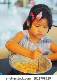 Portrait Of Young Little Girl Mixing Crumbled Crackers And Butter In The Aluminum Bowl For Making Blueberry Cheesecake. Cooking With Kid. Kid Activities Concept.