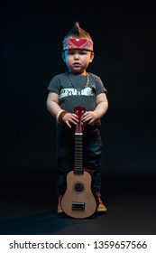 Portrait Of A Young Little Kid Standing With A Guitar On A Black Background And Looking Like A Rock And Roll Star