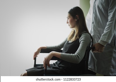 Portrait Of Young Lonely Asian Woman Patient Sitting At Wheelchair In Hospital Room With Her Doctor And Looking Outside White City Copyspace. Paralysis Loss Teen Human Lifestyle Concept