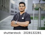 Portrait of young male Asian Arab doctor or student in medical scrubs with stethoscope on the modern college university campus of hospital buildings background