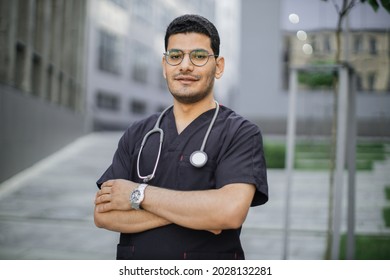 Portrait Of Young Male Asian Arab Doctor Or Student In Medical Scrubs With Stethoscope On The Modern College University Campus Of Hospital Buildings Background