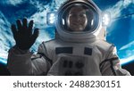 Portrait of Young Male Astronaut Posing in a Space Suit During Spacewalk Outside a Spaceship, Satellite or a Space Station. Spaceman Looking at Camera, Smiling and Waving Hello Gesture with Hand