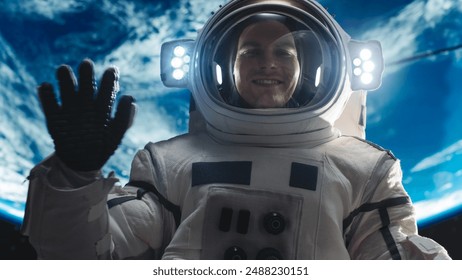 Portrait of Young Male Astronaut Posing in a Space Suit During Spacewalk Outside a Spaceship, Satellite or a Space Station. Spaceman Looking at Camera, Smiling and Waving Hello Gesture with Hand - Powered by Shutterstock