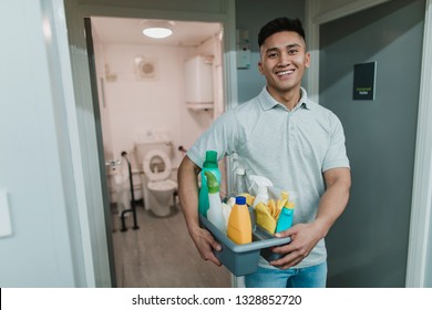 Portrait of a young, male cleaner at work. He is holding a tray of cleaning products.