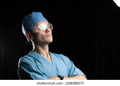 Portrait Of A Young Male Doctor In Uniform And Glasses On A Dark Background.