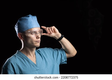 Portrait Of A Young Male Doctor In Uniform And Glasses On A Dark Background.